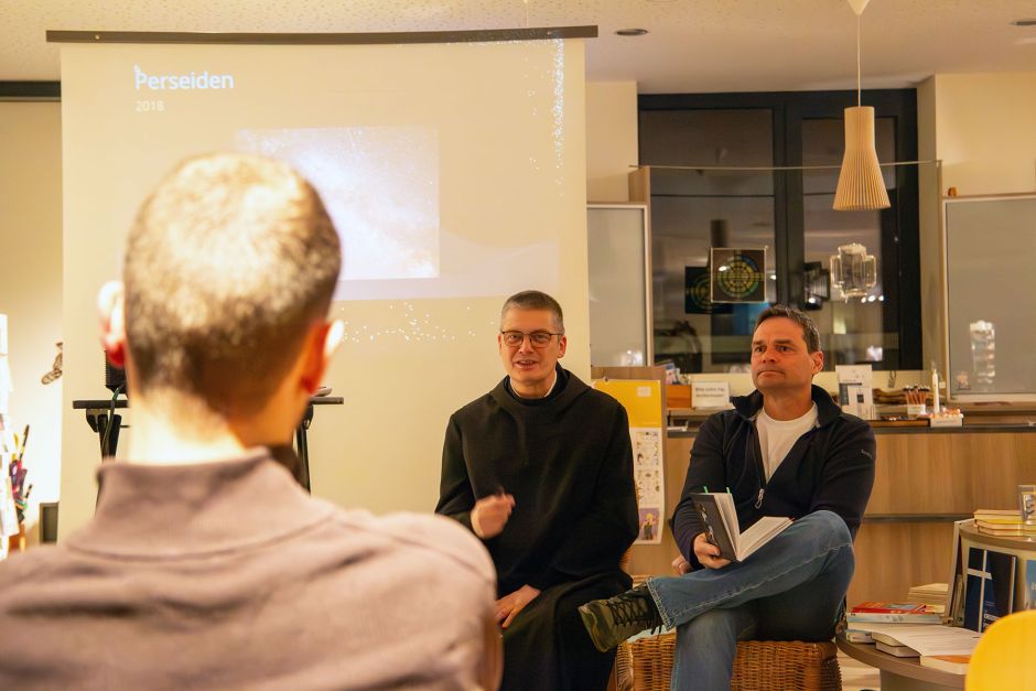 Mann im Habit und Mann in Alltagskleider sitzen in einem Buchladen