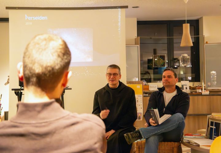 Mann im Habit und Mann in Alltagskleider sitzen in einem Buchladen